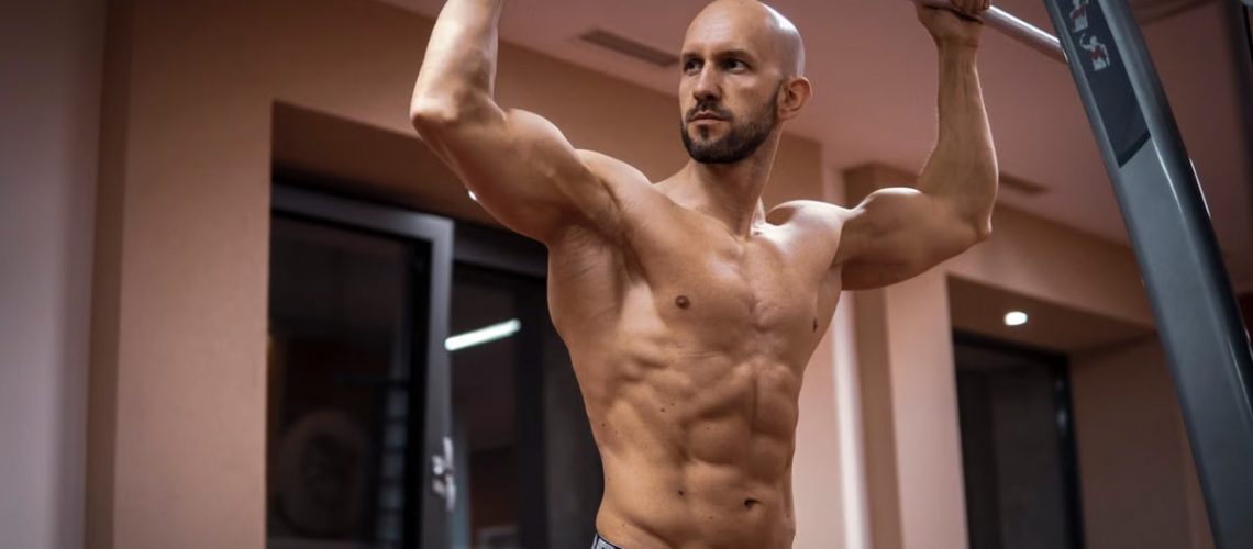 A bald, muscular man performing exercise on gym equipment indoors.